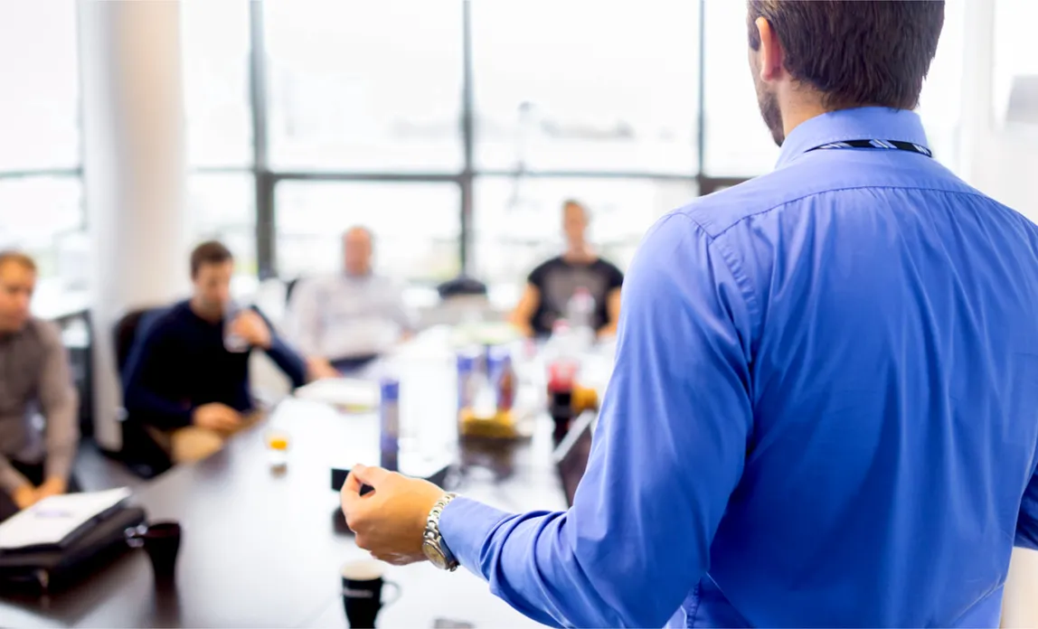 A trainer presenting to a room of people seated at tables